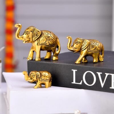 Ascension metal statues featuring three golden elephants with raised trunks sitting on stacked books.
