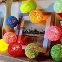 Multicolor rattan ball string lights glowing around photo frames and decorative cat figurines on a shelf