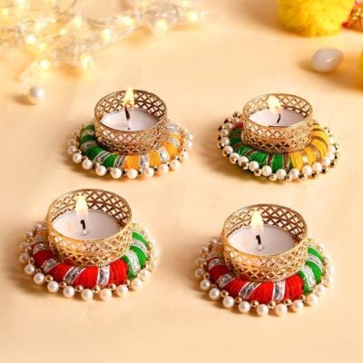 Handcrafted pearl and thread work tealight candle holders with lit candles on a cream background