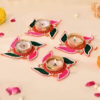 Handcrafted swastik shaped tealight candle holders with pink and green thread work and lit candles on a light surface