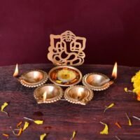 Golden Ganesh Ji Design Urli Bowl for Home with lit oil lamps and floating tealight candle on wooden surface.
