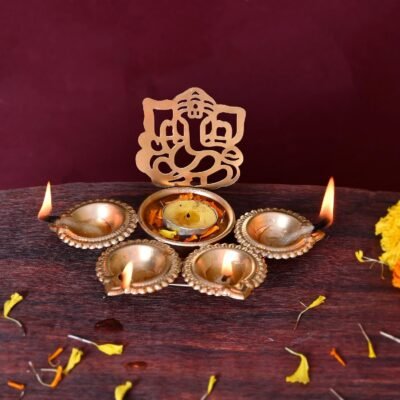 Golden Ganesh Ji Design Urli Bowl for Home with lit oil lamps and floating tealight candle on wooden surface.