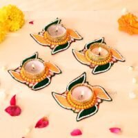 Handcrafted swastik shaped tealight candle holders with green and yellow thread work and lit candles on a light surface