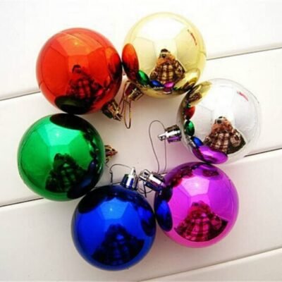 Six multi-color shiny Christmas baubles including red, gold, silver, green, blue, and purple arranged in a circle on a slatted white surface.