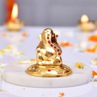 Polished golden brass Lord Ganesha idol studded with red and white stones on a white marble slab