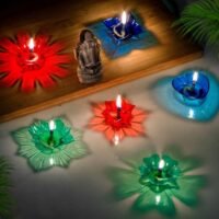 Transform your living space into a glowing spectacle with the Ascension Crystal Water Shadow Diya set. Designers craft these reusable floating oil lamps from high-grade clear acrylic crystal material. This multicolor set features an assortment of lotus flower, star, and heart-shaped diya cups in ruby red, sapphire blue, and emerald green. Fill each cup with water, add a few drops of oil, and light the floating wick. The specially engineered faceted bottom projects mesmerizing, starburst-shaped colorful light patterns across your floor or wooden table. Their lightweight heat-resistant design ensures safe, clean burning for long festive evenings without smoke or wax mess. Place them alongside Lord Ganesha idols, festive rangoli designs, entrance balconies, and pooja altars during Diwali, Navratri, and wedding celebrations. Bring magical light reflections and enchanting festive charm to your space with Ascension floating glass decor!