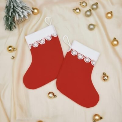 Two red lace Christmas stockings with white cuffs resting on a cream fabric surrounded by gold baubles.