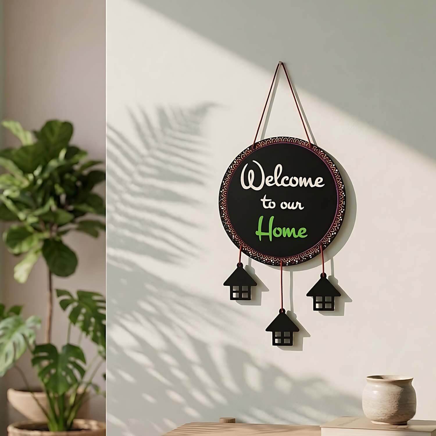 Circular black Welcome Home Wall Hanging with decorative house cutouts hanging below on a light wall.