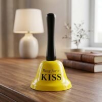 Yellow hand bell with black handle printed with Ring for a KISS text on a wooden table