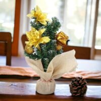 A miniature gold decorated Christmas tree with a burlap base sitting on a wooden table next to a natural pinecone.