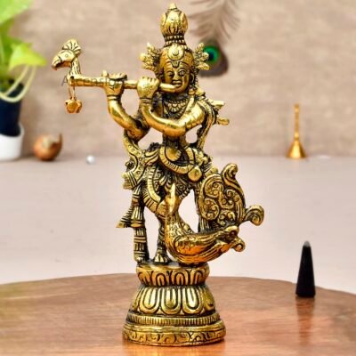 Golden brass Krishna idol playing flute standing on lotus base next to a peacock