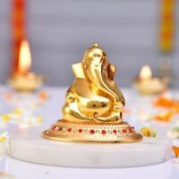 Glossy golden brass Ganesha idol with stone studded circular base on a white marble slab