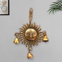 Golden brass Surya Sun face wall hanging with three hanging bells mounted on a grey wall