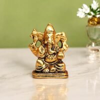Antique golden brass small Ganesha idol seated on a rectangular base on a marble table