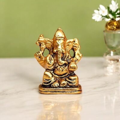 Antique golden brass small Ganesha idol seated on a rectangular base on a marble table