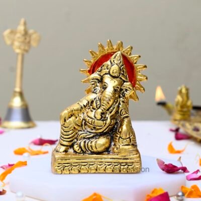 Golden brass Ganesha idol with red sun halo background on a white marble slab