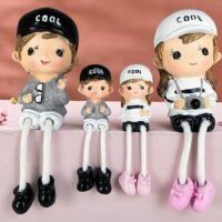 Ascension 4 piece family dangling leg showpiece set featuring four cute resin dolls with COOL caps sitting on a pink shelf.
