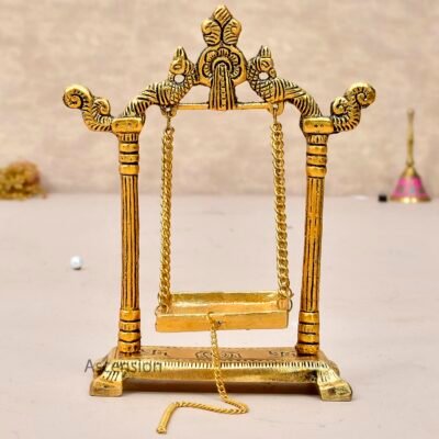 Golden brass Laddu Gopal jhula swing with peacock carvings and pull chain on a light table