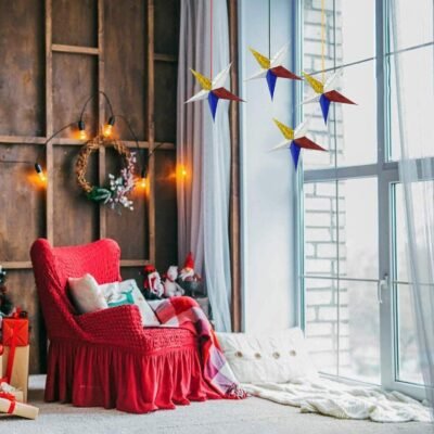 Four 3D multicolor hanging star ornaments displayed in a cozy, festive living room by a large window.