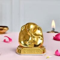 Glossy golden brass Ganesha idol with Om Ganeshay Namah inscribed base on a pink table