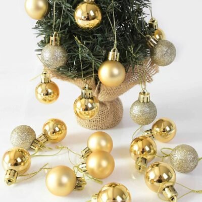 Several small gold Christmas baubles featuring shiny, matte, and glitter finishes scattered around a miniature pine tree.