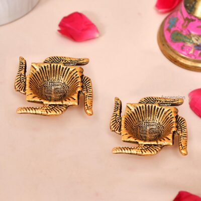 Pair of golden brass Swastik shaped diyas with engraved Swastik symbols inside oil cups on a light surface