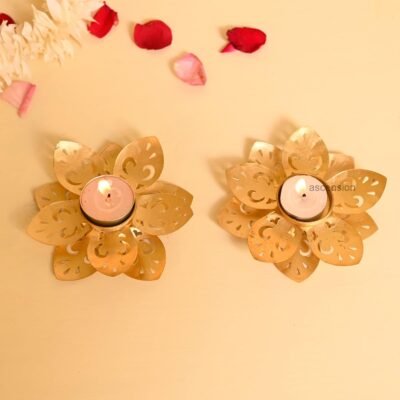 Two golden lotus tealight candle holders with burning tealights on a beige background with rose petals