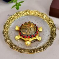 Golden brass tortoise showpiece with red beads sitting in a decorative brass rimmed dish
