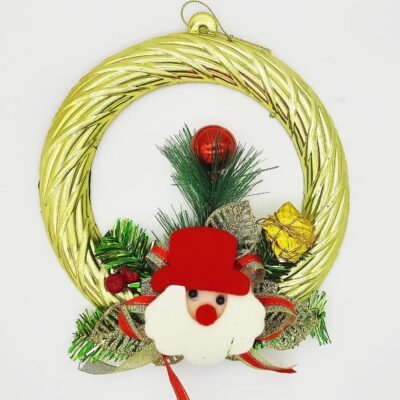 A gold Christmas wreath ornament decorated with a plush Santa Claus face, green pine sprigs, a red bauble, and a gold gift box on a white background.