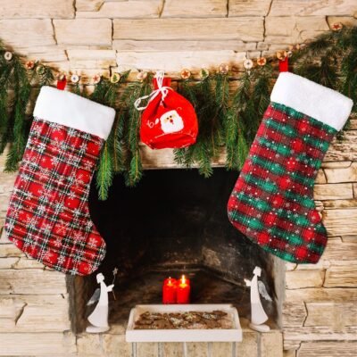Two plaid Christmas stockings with white cuffs hanging on a stone fireplace mantel decorated with pine garland.