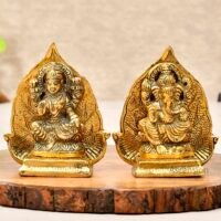 Golden brass Goddess Lakshmi and Lord Ganesha idol set with peepal leaf backdrop on wooden slab