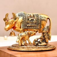 Golden brass Kamdhenu cow and calf idol with decorative blanket and hanging bell on a wooden surface