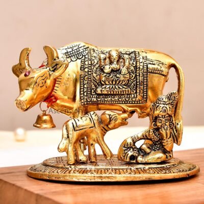 Golden brass Kamdhenu cow and calf idol with decorative blanket and hanging bell on a wooden surface