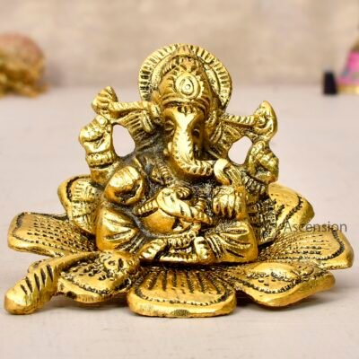 Golden brass Lord Ganesha idol seated on a carved leaf base on a white surface
