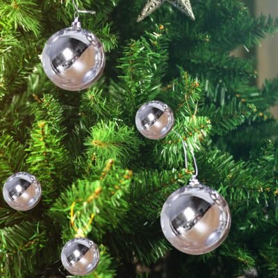 Several clear plastic Christmas tree baubles with silver caps hanging on the green branches of an artificial pine tree.