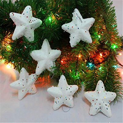 Six white frosted star ornaments with colorful confetti hanging on a lit Christmas tree and resting on a surface.