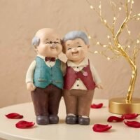 Ascension old couple showpiece featuring a smiling elderly couple standing arm in arm on a table with red rose petals.