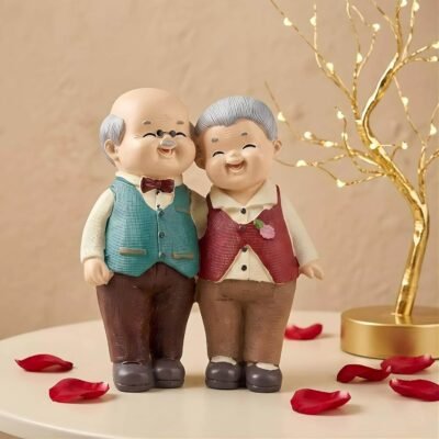 Ascension old couple showpiece featuring a smiling elderly couple standing arm in arm on a table with red rose petals.