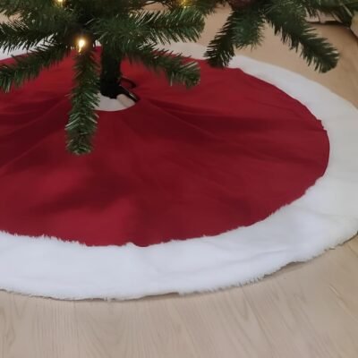 A red Christmas tree skirt with a white faux fur trim wrapped around the base of a lit pine tree on a wooden floor.