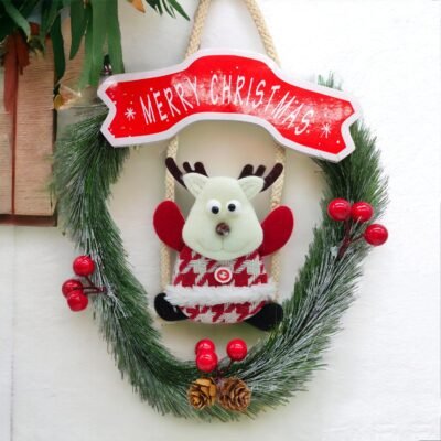A frosted green pine Christmas wreath featuring a red Merry Christmas banner and a plush reindeer sitting on a swing.