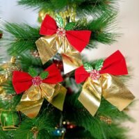 Three red and gold Christmas tree bows with green holly leaves hanging on a pine tree.