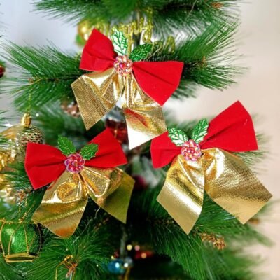 Three red and gold Christmas tree bows with green holly leaves hanging on a pine tree.
