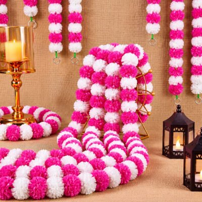 Pink Artificial Marigold Garlands pack of 5 displayed with pink and white artificial pom-pom flowers alongside lanterns and candle holders on a burlap backdrop.