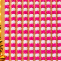 Pink Marigold Garland Strings pack of 10 hung vertically side by side as a full wall backdrop with pink and white pom-pom flowers.