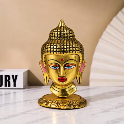 Golden Buddha head statue with colorful hand-painted details displayed on a sleek dark shelf next to decorative books.