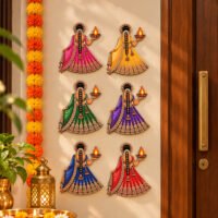 Set of six colorful Indian women wall hangings wearing lehengas and holding glowing oil lamps beside a wooden entrance door.