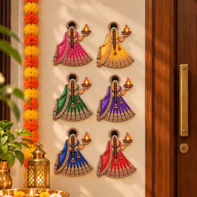 Set of six colorful Indian women wall hangings wearing lehengas and holding glowing oil lamps beside a wooden entrance door.