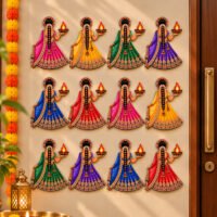 Set of twelve vibrant Indian lady wall cutouts dressed in colorful lehengas while holding glowing diya lamps beside a main door.