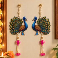 Pair of handcrafted peacock wall hanging ornaments with pearl strands and pink tassels on a beige wall.