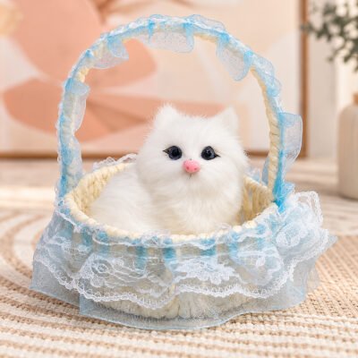 A realistic white plush kitten with a pink nose sits inside a light beige woven basket with blue lace trim.